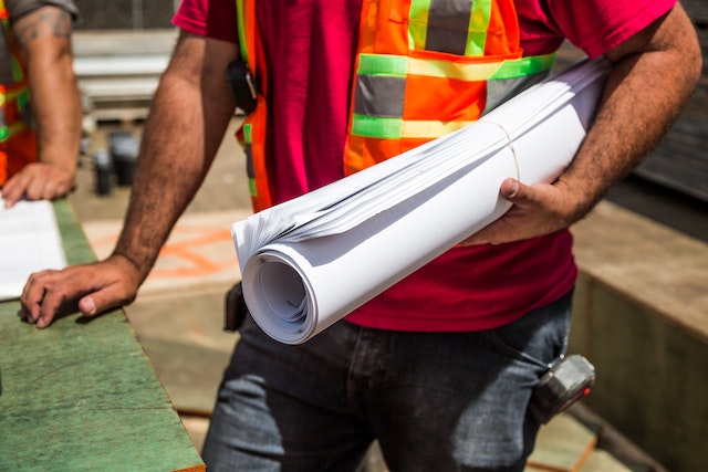 person in orange reflective vest holding a large rolled up paper